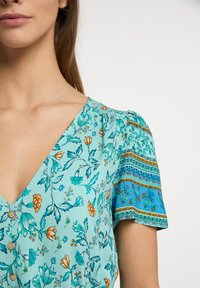 Blumenmuster-Kleid in hellem Blaugrün mit orangefarbenen und grünen Akzenten. Verfügt über einen V-Ausschnitt, Knopfdetail und gemusterte Puffärmel.