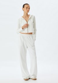 Witte cropped zip-up hoodie met trekkoorden, gecombineerd met losse witte sweatpants met een zijzak en elastische tailleband.