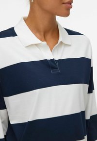 Polo a maniche lunghe a righe navy e bianche in cotone. Presenta un colletto classico e cuciture a vista sulla patta.