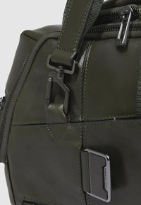 Borsa in pelle verde scuro dalla superficie liscia, con una robusta fibbia in metallo nero, cuciture a contrasto e una ferramenta rettangolare di fissaggio.