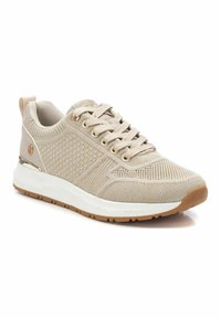 Chaussure de sport beige avec une tige en maille texturée, fermeture à lacets et une semelle intermédiaire blanche contrastante. Présente des accents métalliques et une semelle extérieure en caoutchouc.