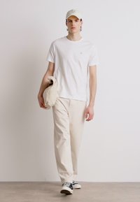 Hvit bomull t-skjorte, beige bomullsstrømpebukser, grå joggesko og en lyseferdig cap. Outfiten har et enkelt, avslappet design.