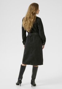 Robes en denim noir avec une taille ceinturée, des manches longues et un ourlet jusqu'aux genoux. Associée à des bottes noires montantes. Texture lisse.