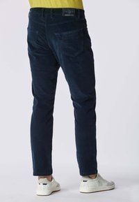 Pantaloni in corduroy blu navy con vestibilità slim, dotati di due tasche posteriori e passanti per cintura. Abbinati a sneakers bianche, che mettono in risalto una texture liscia.
