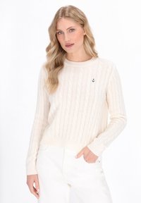 Sweter w kolorze kremowym, pleciony, z okrągłym dekoltem, ściągaczami na mankietach oraz haftowanym detalem w kształcie kotwicy na lewej piersi. W zestawieniu z białymi spodniami.