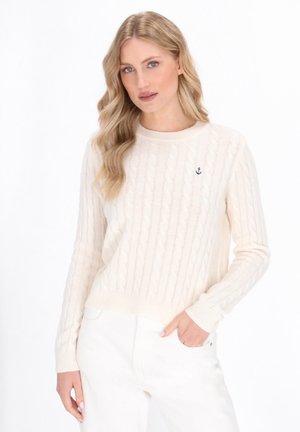 Crème kleurige kabelgebreide trui met een ronde halslijn, geribbelde mouwen en een geborduurd ankerdetail op de linker borst. Gemaakt met witte broek.