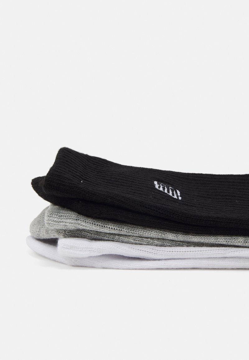 Trois paires de chaussettes empilées : noires, grises et blanches. Texture côtelée avec un branding subtil sur la chaussette noire. Matière en mélange de coton.
