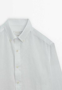 Vit linneskjorta med knappkrage, utrustad med en knappslå fram med ljusfärgade knappar och ett mjukt, texturerat tyg.