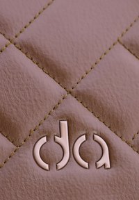 Superficie de cuero acolchado en rosa suave, con un logotipo en relieve en un tono más claro, acentuado con costuras amarillas para detalles.