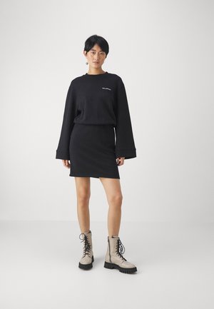 Čierna oversize mikina so širokými rukávmi, skombinovaná s priliehavou čiernou mini sukňou. Model má na sebe svetlošedé bojové čižmy s čiernymi šnúrkami.