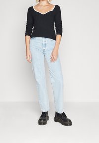 Zwarte geribbelde langemouwen top met een V-hals en witte bies, gecombineerd met lichtblauwe high-waisted jeans en zwarte veterschoenen.