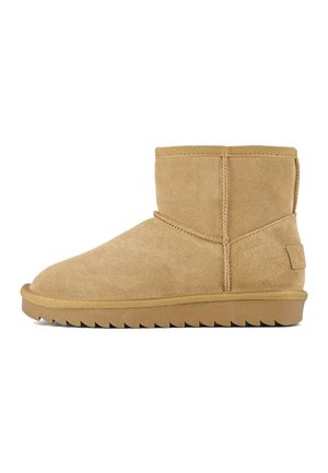 Bottines en suede tan avec un orteil arrondi, une semelle plate et des détails de couture subtils. La semelle présente un motif de semelle en zigzag pour une meilleure adhérence.