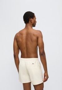 Μπεζ μαγιό σορτς από ελαφρύ ύφασμα, με ελαστική μέση και πίσω τσέπη με κάθετη λεπτομέρεια σε κόκκινο, λευκό και μπλε.