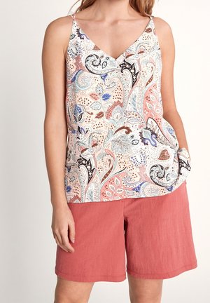 Kvinde iført ærmeløs V-hals top med blomstret paisleymønster i pink, blå og brune farver, kombineret med løstsiddende koralrosa shorts.