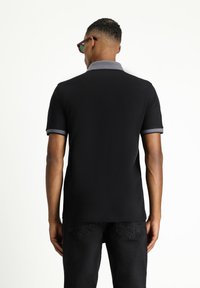Schwarzes Poloshirt mit einem grauen Kragen und Ärmeln. Kurze Ärmel und ein gerader Saum. Der Stoff wirkt glatt und leicht.