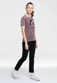 Grau-lila Baumwoll-T-Shirt mit einem Aufdruck eines Cartoon-Pinguins, getragen mit schwarzen Jeans und weißen Sneakern.