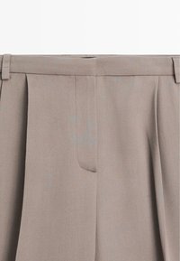 Plisserede beige bukser med fladt frontdesign, subtil struktur og sidelommer integreret i linningen.