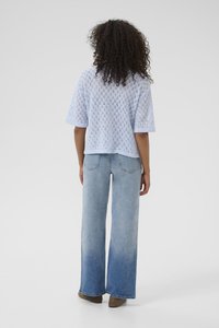 Haut tricoté bleu clair à manches courtes avec un motif en losange. Associé à un jean taille haute à jambes larges en denim clair et des bottines brunes.