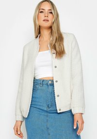 Giacca bianca con trama, colletto rotondo, chiusura a bottoni e polsini elasticizzati, abbinata a un top bianco aderente e una gonna di jeans blu.