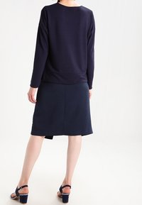Top de manga larga azul marino y falda hasta la rodilla, hecha de tela suave. El top presenta un cuello redondo; la falda tiene un corte recto con una abertura en la parte posterior.