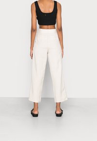 Czarny, krótki top na ramiączkach z szerokimi, wysokim stanem beżowymi spodniami z lnu. Gładka tekstura, minimalistyczny design i szczegół z odkrytymi plecami.