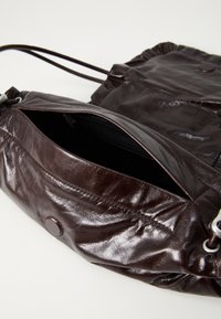 Dark brown leather drawstring bag with open zippered compartment and magnetic snap closure on a light background.