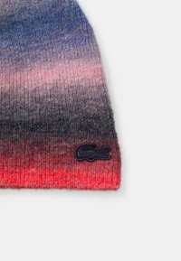 Gorro de punto con un patrón de color en degradado que va del gris al rojo, con un acabado texturizado y un parche de logo en azul marino en el lateral.