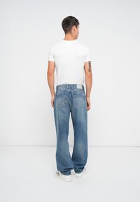 Jeans de mezclilla de color azul claro, holgados, con ligeros detalles desgastados y corte recto, combinados con una camiseta blanca sencilla y zapatillas.