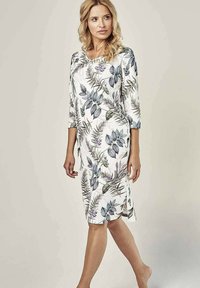 Kwiecista sukienka do kolan z białym tłem i wzorami zielonych i fioletowych liści, wykonana z miękkiego materiału o luźnym kroju.