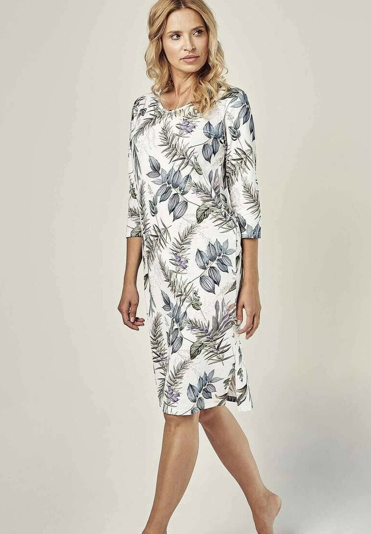 Kwiecista sukienka do kolan z białym tłem i wzorami zielonych i fioletowych liści, wykonana z miękkiego materiału o luźnym kroju.