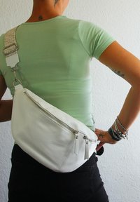 Weiße Leder-Crossbody-Tasche mit strukturierter Oberfläche, ausgestattet mit einer Reißverschlusstasche und verstellbarem gemustertem Gurt.