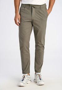 Pantalons kaki cintrés avec taille à cordon, deux poches latérales et texture subtile. Portés avec des baskets blanches aux accents colorés.