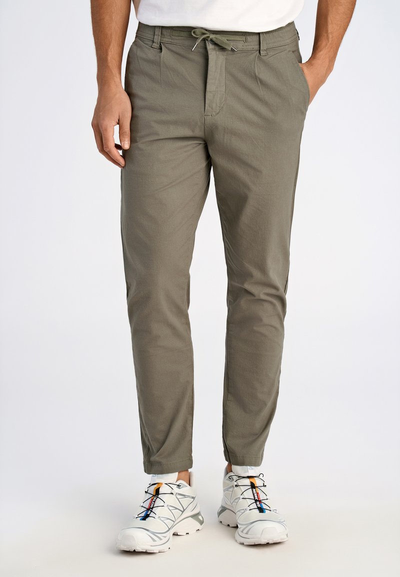 Pantalons kaki cintrés avec taille à cordon, deux poches latérales et texture subtile. Portés avec des baskets blanches aux accents colorés.