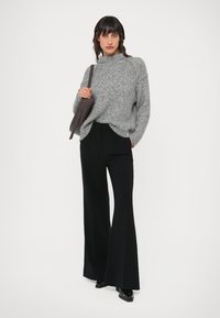 Oversized grey knitted sweater with a high neckline paired with black flared trousers, featuring a smooth texture and a tailored fit.