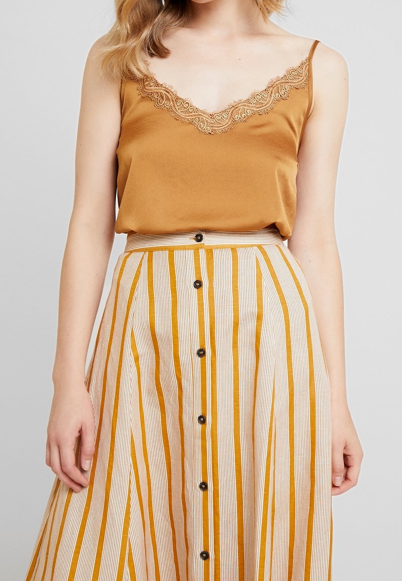 Top in cotone color senape con pizzo, abbinato a una gonna A-line a righe in crema e ambra, con bottoni frontali e una vita in risalto.