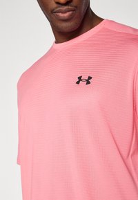 Ροζ αθλητική μπλούζα με κοντά μανίκια, με υφασμένο σχέδιο και μαύρο λογότυπο Under Armour στο στήθος.