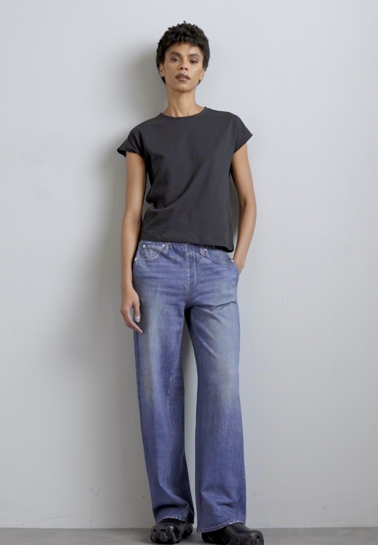 Haut noir à manches courtes associé à un jean large bleu clair et des sabots noirs. Tissu en coton doux ; coupe décontractée ; détails de design minimaux.