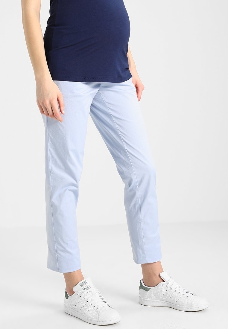 Chinos bleu clair à coupe droite, en coton. Portés avec des baskets blanches ornées d'accents verts et un haut bleu marine.