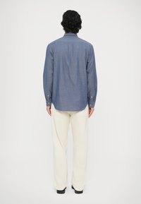 Koszula dżinsowa w jasnoniebieskim kolorze, z długimi rękawami i plisą na guziki, zestawiona z kremowymi spodniami. Gładka tekstura, klasyczny krój.