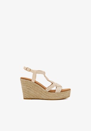 Sandalia de cuña beige con tiras trenzadas, hebilla en el tobillo y plataforma con suela de cuerda tejida.