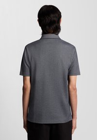 Grå polo t-shirt med krave og korte ærmer, der har en glat tekstur og subtile syningsdetaljer ved halsudskæringen og kanten.