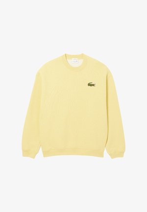 Sudadera amarilla de tejido suave, con cuello redondo, mangas largas y un pequeño logo de cocodrilo verde en el lado izquierdo del pecho.