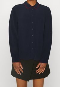 Dunkelblaues Hemd mit langen Ärmeln und Knopfleiste, mit kontrastierenden roten Akzenten am Kragen und an den Manschetten, aus einem glatten, leichten Stoff gefertigt.