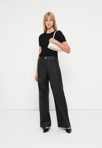 Top negru ajustat combinat cu blugi negri cu picioare largi, completat de o geantă crem pentru umăr și pantofi negri cu bot ascuțit. Texturi netede, design minimalist.