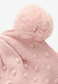 Bonnet tricoté rose avec un large pompon en fourrure sur le dessus et des points texturés sur tout le corps pour plus de détail.