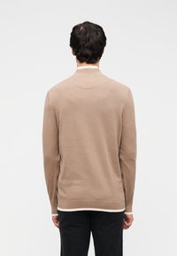 Pull en maille beige avec un col côtelé, des manches longues et des fentes latérales. Présente une bordure claire contrastante à l'ourlet. Texture douce.