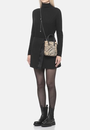 Donna con dolcevita nero, gonna nera, collant neri trasparenti, stivali neri e borsa con stampa zebre con manici neri e tracolla a catena.