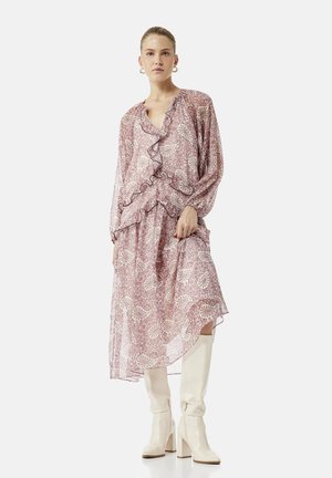 Mujer con vestido midi rosa con estampado paisley, volantes y botas blancas altas con tacón, posando frente a un fondo liso.