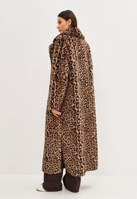 Abrigo de piel sintética con estampado de leopardo, con un amplio cuello, mangas largas y aberturas laterales. El material parece suave y texturizado.