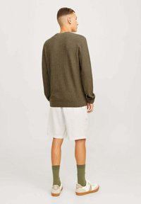 Pull en tricot vert olive avec des manches longues, un col rond et une coupe décontractée, associé à un short clair et des baskets blanches avec des semelles brunes.